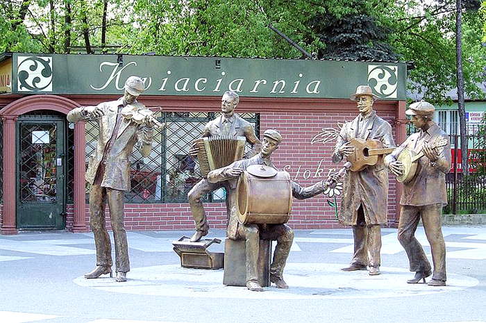 Skrzypek, akordeonista, gitarzysta, bandżolista i bębniarz wchodzą w skład kapeli uwiecznionej w pomniku autorstwa rzeźbiarza Andrzeja Renesa 